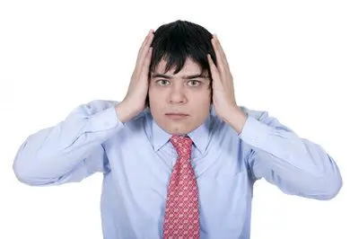 A man in a light blue shirt and red patterned tie holds his hands to the sides of his head, looking directly at the camera with a concerned or stressed expression against a white background.